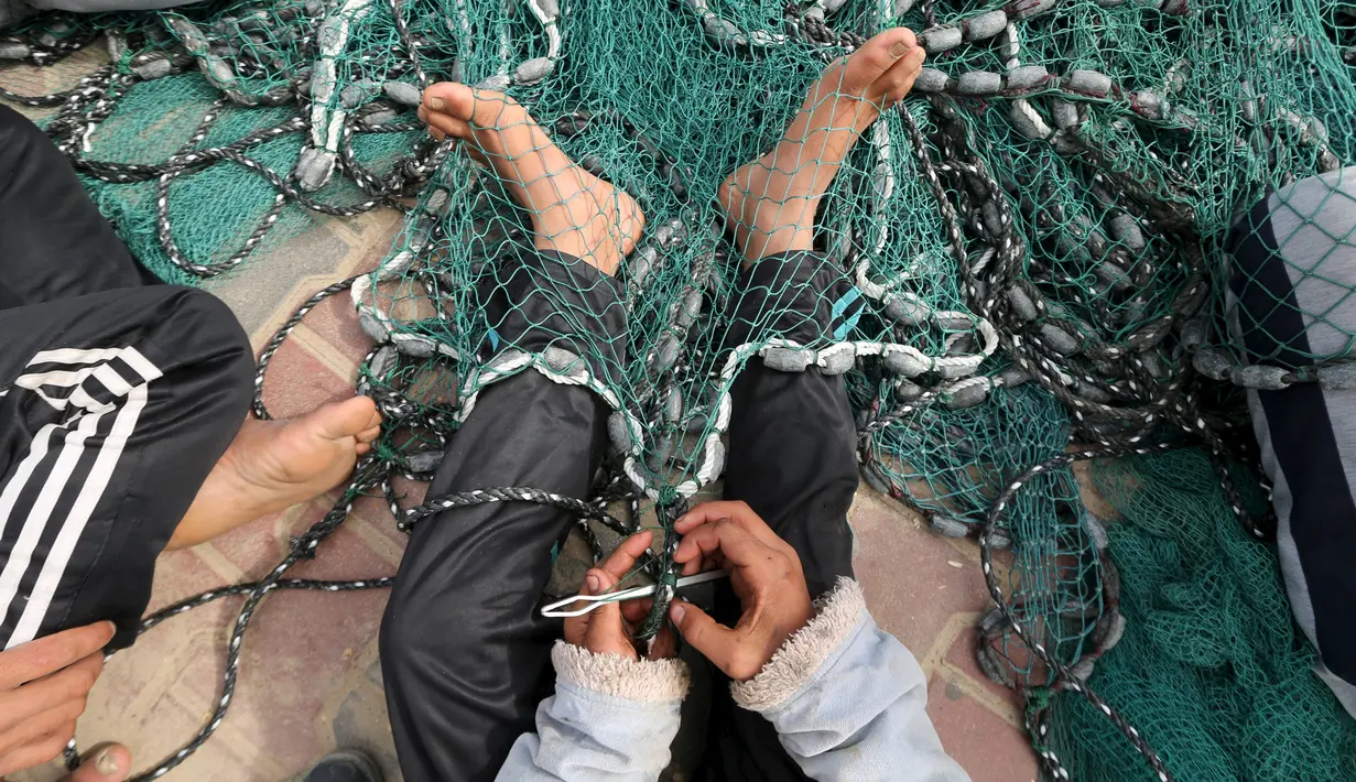 Mohammad al-Asi (16), anak Palestina memperbaiki jaring ikan di Pelabuhan Kota Gaza, (29/3). Bocah yang putus sekolah sejak dua tahun lalu, ikut membantu orang tuanya untuk mencari rezeki dengan cara bernelayan bersama ayahnya. (REUTERS/Mohammed Salem)