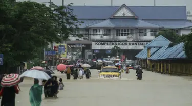 Warga menerobos banjir yang menggenangi jalanan di depan Kantor imigrasi dan bea cukai di Rantau Panjang, Selasa (3/1). Akibat hujan lebat yang turun terus menerus selama empat hari di Malaysia, 5000 warga terpaksa dievakuasi. (AFP PHOTO/STR/Malaysia OUT)