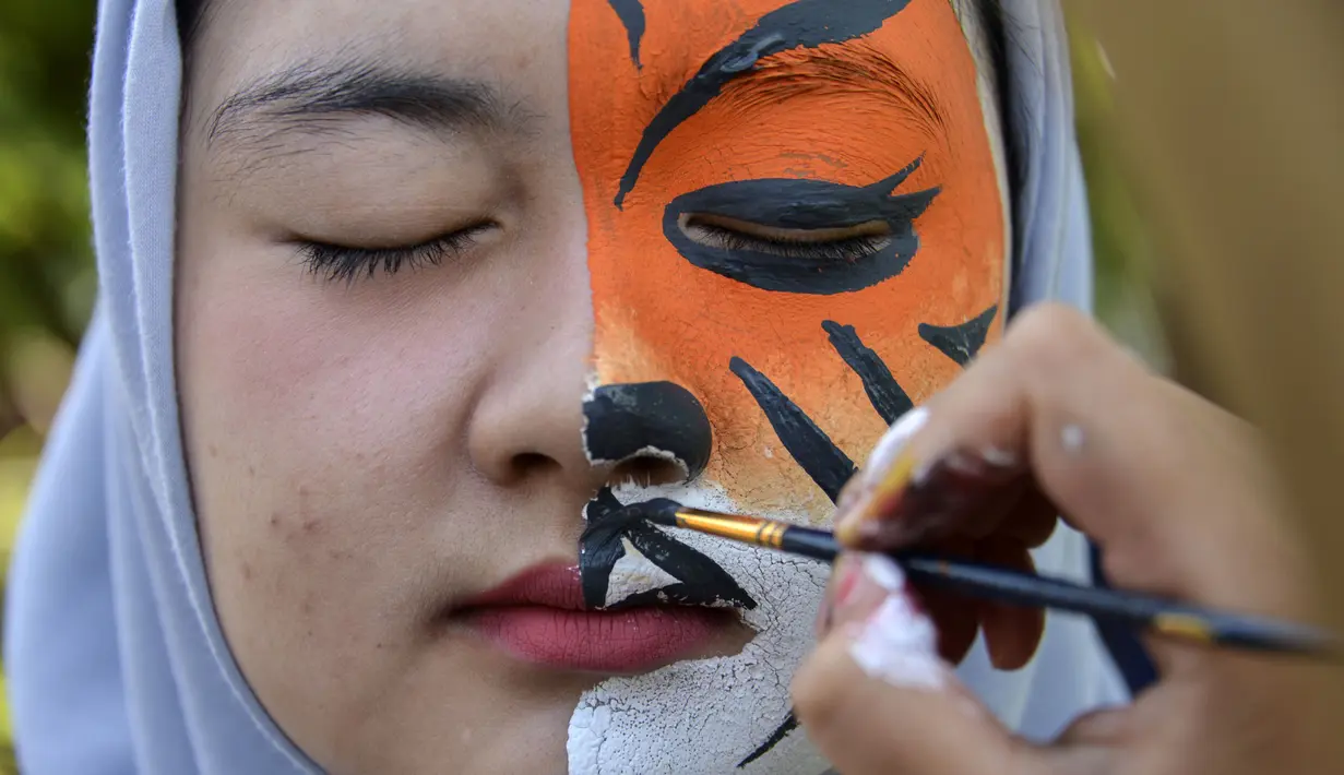 Seorang pelajar dilukis wajahnya dengan gambar harimau saat melakukan aksi demonstrasi dalam peringatan Hari Bumi di Banda Aceh (22/4). Dalam aksinya para pelajar tersebut membuat karya-karya berupa gambar satwa Indonesia, seperti, orangutan, gajah dan harimau. (AFP Photo/Chaideer Mahyuddin)