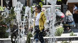 Seorang pejalan kaki berjalan di jalan mengenakan masker pelindung di pusat Thessaloniki, Yunani utara (18/5/2022). Sebuah komite ahli dari Kementerian Kesehatan sedang memeriksa kemungkinan melonggarkan mandat masker pada 1 Juni, menyusul penurunan Covid19. (AFP/Sakis Mitrolidis)