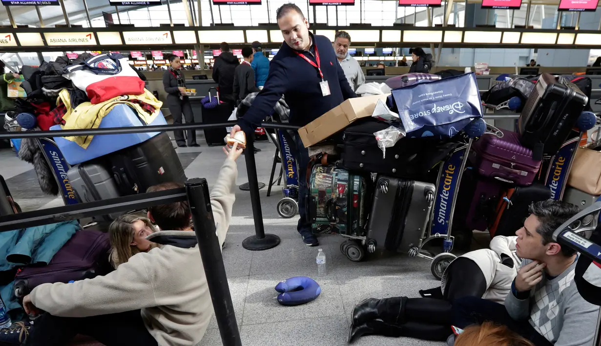 Petugas maskapai Avianca membagikan makanan untuk penumpang saat menunggu penerbangan yang tertunda di Bandara John F Kennedy (JFK), New York, Senin (8/1). Penundaan sejumlah penerbangan akibat banjir mengakibatkan penumpang terlantar. (AP/Richard Drew)