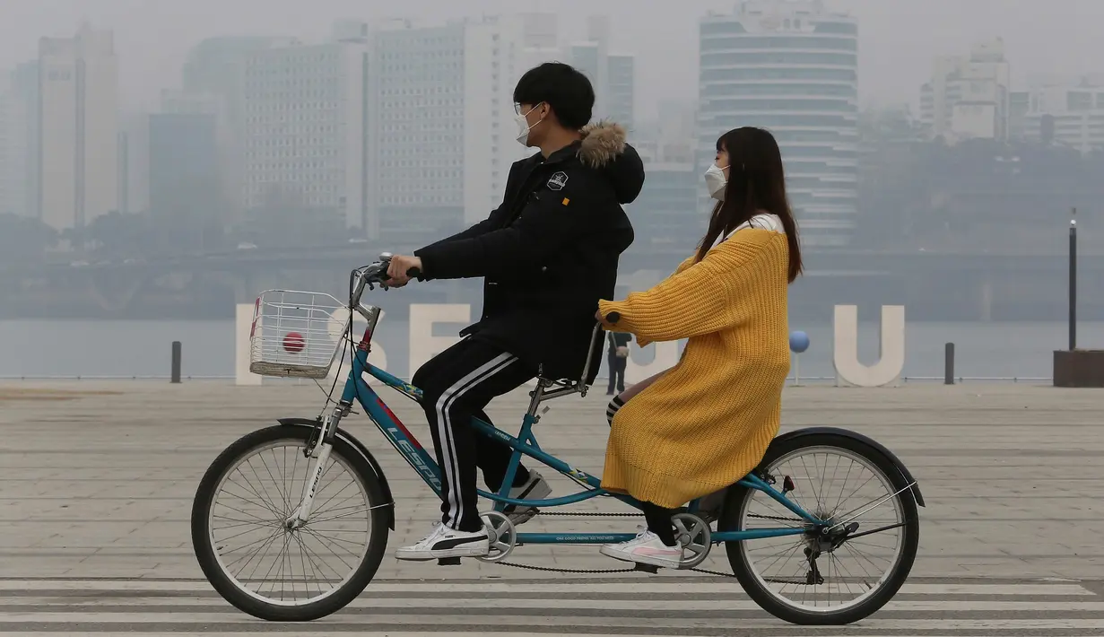 Pasangan naik sepeda menggenakan masker saat pemandangan kota diselimuti kabut tebal partikel debu halus di Seoul, Korea Selatan (5/3). Kementerian Lingkungan Korsel mengeluarkan langkah-langkah penurunan debu halus darurat. (AP Photo/Ahn Young-joon)