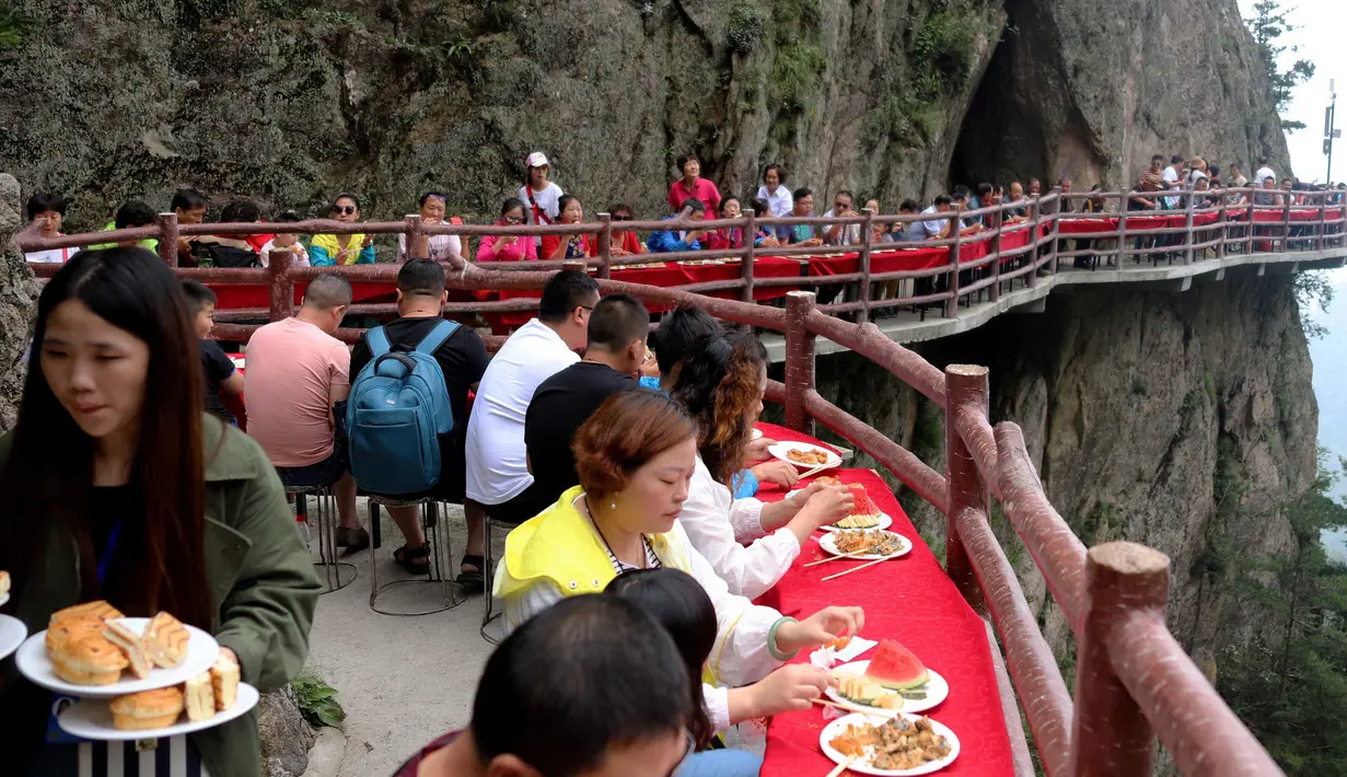 Wisatawan menyantap makanan pada acara perjamuan di sepanjang tepi tebing di Laojun Mountain provinsi Henan, China. Wisatawan menikmati berbagai suguhan makanan di jalanan selebar enam kaki yang menempel pada tebing setinggi 2.000 meter. (AFP)