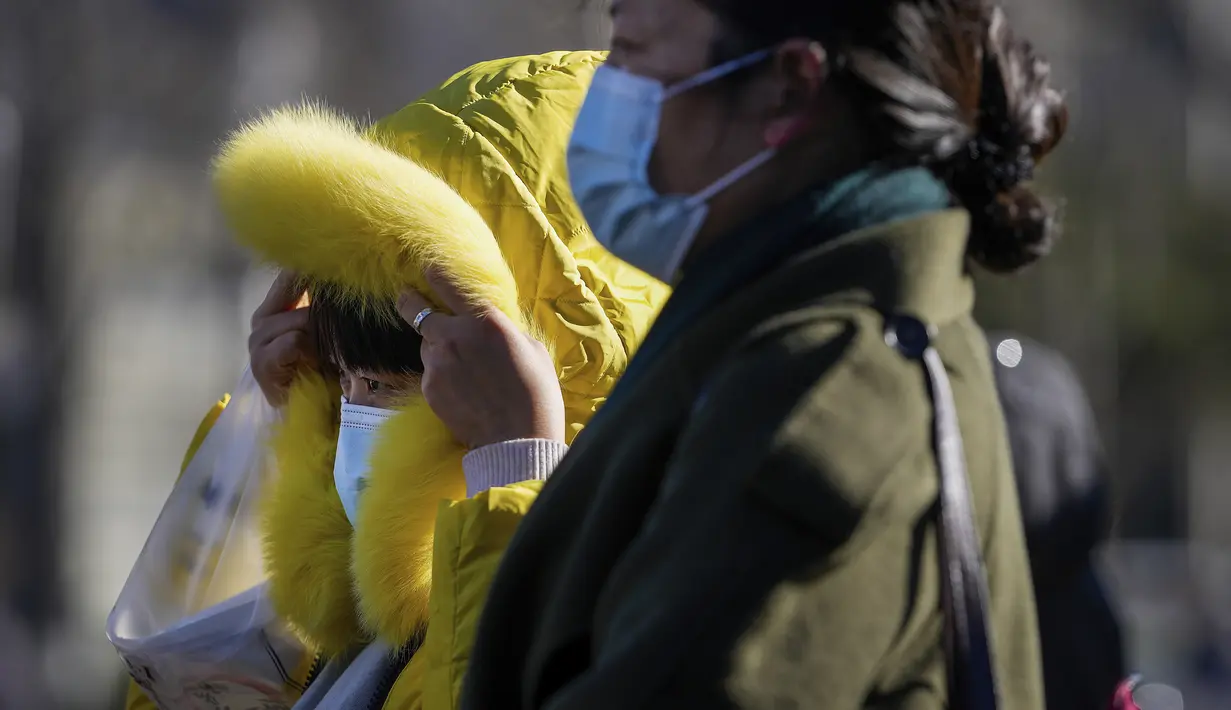 Seorang wanita yang mengenakan masker untuk membantu mengekang penyebaran virus corona mengenakan tudung bulunya saat berjalan di distrik perbelanjaan Wangfujing saat ibu kota dilanda angin dingin di Beijing, Minggu (12/12/2021).  (AP Photo/Andy Wong)