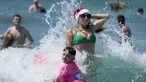 Pengunjung asal Inggris Sophie Woodward (kanan) mengenakan topi Santa saat bermain di air bersama sepupunya Maxi Woodward di Pantai Bondi di Sydney, Senin, 25 Desember 2023. (AP Photo/Rick Rycroft)
