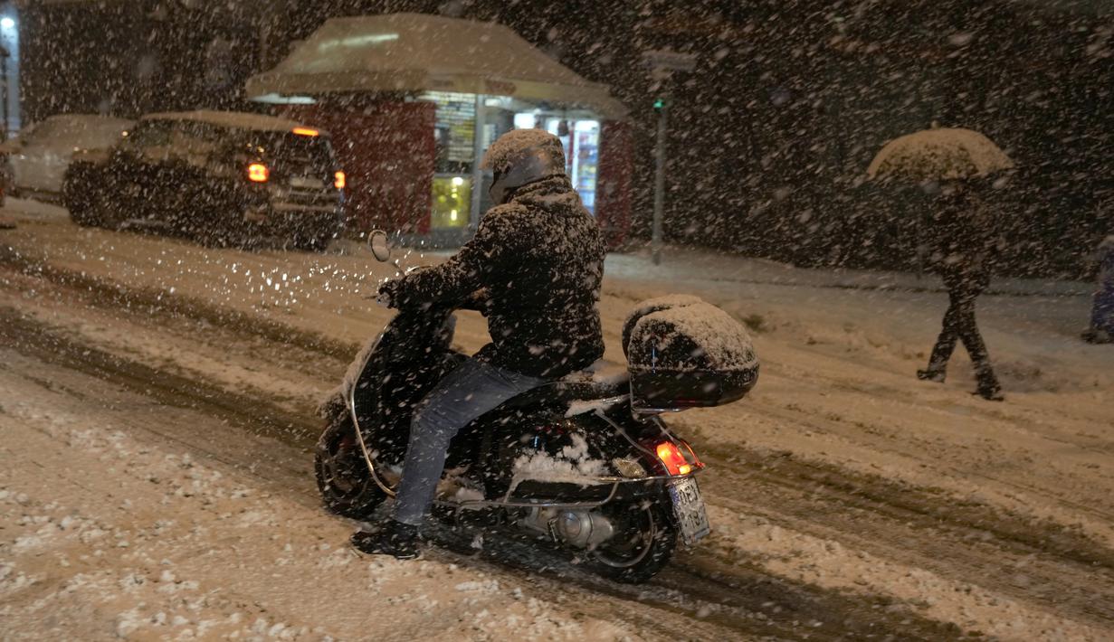 Seorang pria mencoba berkendara di jalan yang tertutup salju selama badai salju di Athena, Yunani, Senin (24/1/2022). Hujan salju lebat mengganggu lalu lintas udara di ibu kota Athena dan kota tetangga terbesar Turki, Istanbul. (AP Photo/Thanassis Stavrakis)