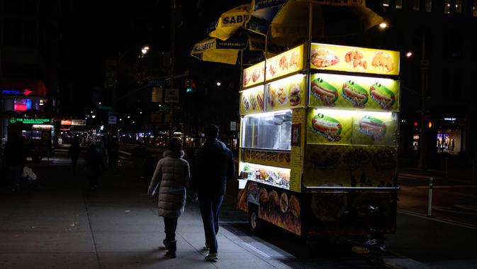 Pejalan kaki melewati gerobak makanan di New York, Senin (16/3/2020). Tiga wilayah juga akan membatasi kapasitas kerumunan untuk pertemuan sosial dan rekreasi hingga 50 orang. (AP Photo/Yuki Iwamura)