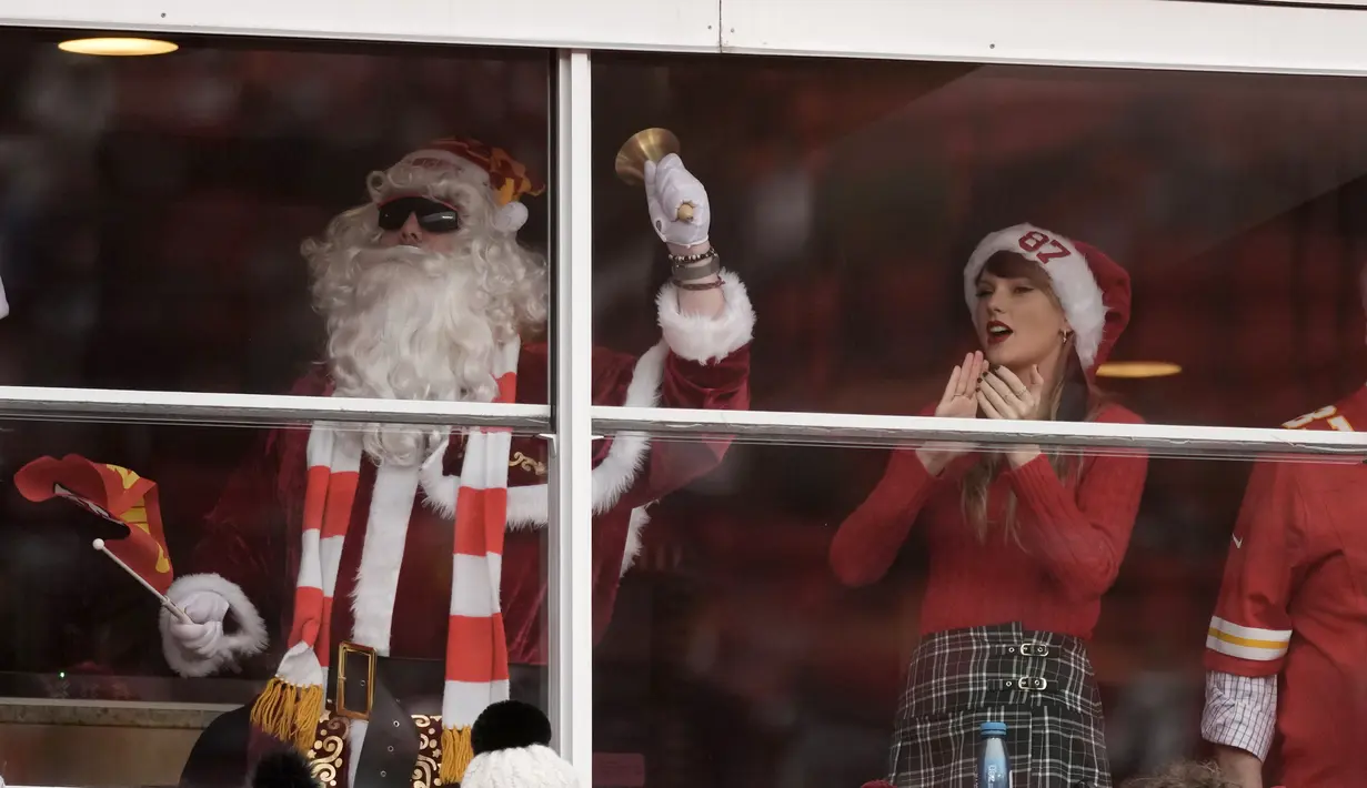 Taylor Swift memadukan nuansa Natal dengan mengenakan sweater merah dan plaid miniskirt serta topi Santa bertulisan 87. Itu adalah nomor punggung Travis Kelce. (AP Photo/Charlie Riedel)