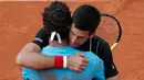 Petenis Serbia, Novak Djokovic memeluk petenis Italia Marco Cecchinato seusai perempatfinal Prancis Terbuka 2018 di stadion Roland Garros, Selasa (5/6). Djokovic tumbang 3-6, 6-7, 6-1, dan 6-7 dalam waktu 3 jam 26 menit. (AP Photo/Michel Euler)