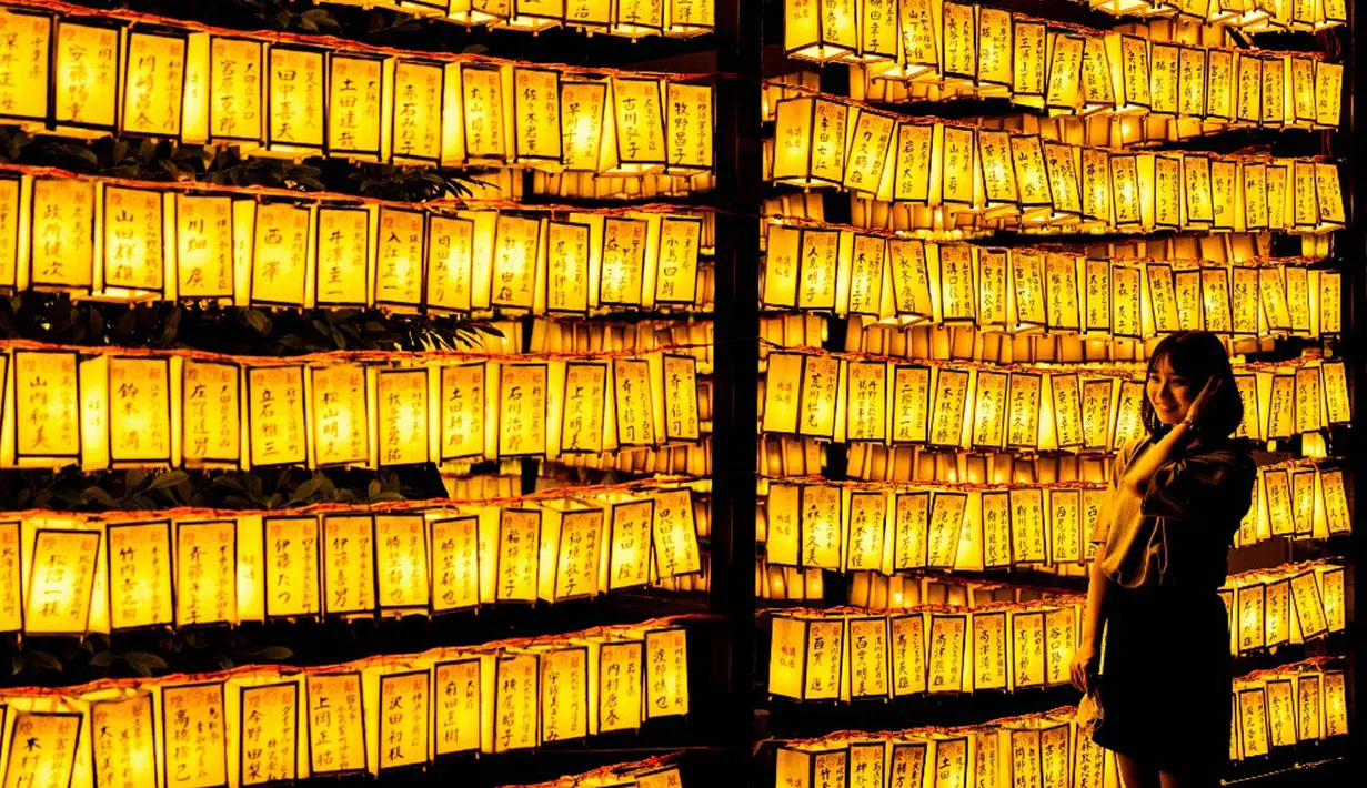 Pengunjung berpose untuk foto dengan lentera kertas saat Festival Mitama di Kuil Yasukuni, Tokyo, Jepang, Rabu (14/7/2021). Festival Mitama dirayakan sejak 1947 untuk menghormati jiwa para arwah yang diabadikan serta tentara yang gugur dari perang Jepang di masa lalu. (BEHROUZ MEHRI/AFP)