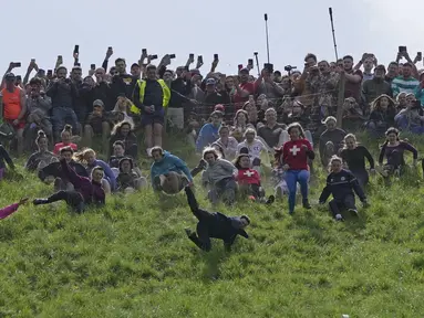 Para peserta bersaing dalam perlombaan menuruni bukit putri selama kontes Cheese Rolling di Cooper's Hill di Brockworth, Gloucestershire, Senin 29 Mei 2023. (AP Photo/Kin Cheung)