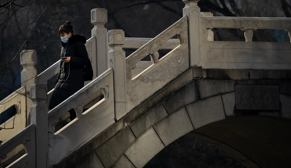 Seorang wanita berjalan melintasi jembatan penyeberangan di taman umum di Beijing, Rabu (5/1/2022). China melaporkan penurunan besar infeksi COVID-19 lokal di kota utara Xi'an, yang telah dikunci ketat selama dua minggu terakhir. (AP Photo/Mark Schiefelbein)