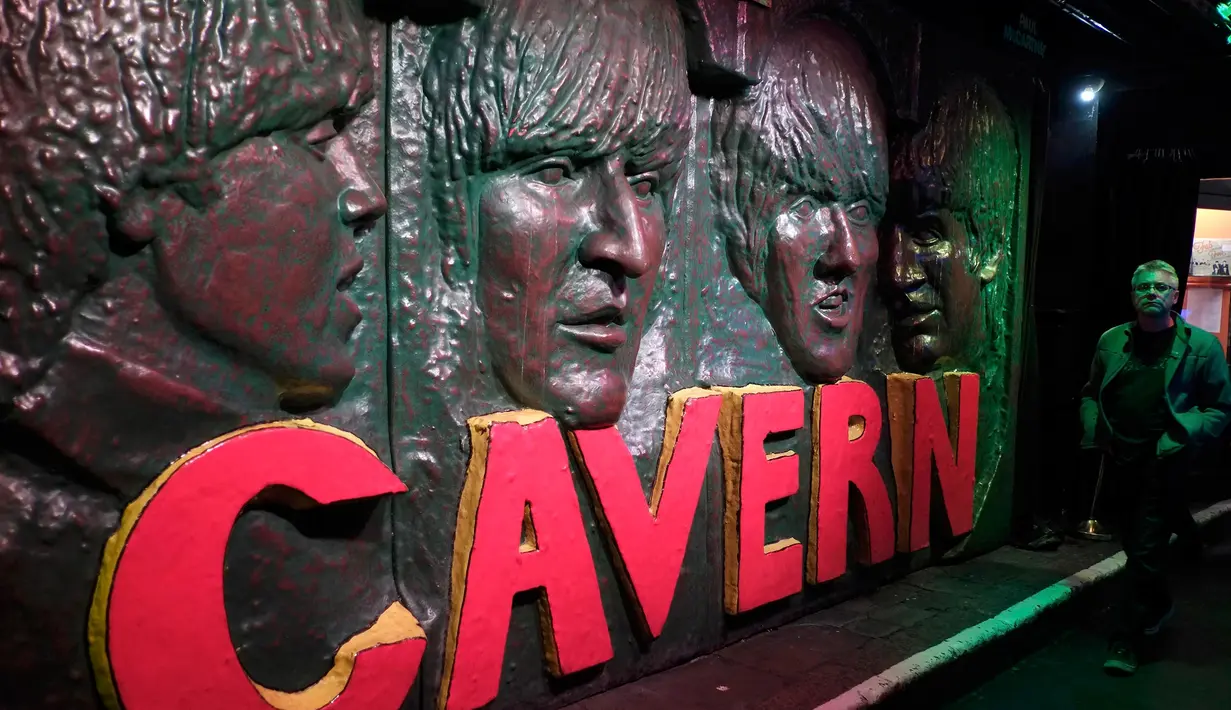 Seorang pria berjalan melewati patung wajah personel The Beatles  di Liverpool, Inggris, (16/8). Kota Liverpool  tiap tahunnya menadapat 105 juta dollar dari para penggemar The beatles dari seluruh dunia yang hadir ke kota ini. (REUTERS/Phil Noble)