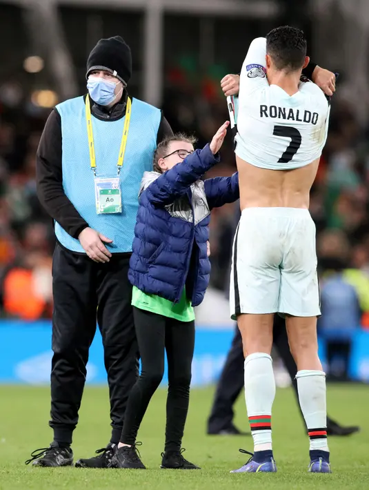 Striker Portugal Cristiano Ronaldo melepas jerseynya untuk fans cilik pada akhir laga Grup A Kualifikasi Piala Dunia 2022 Zona Eropa melawan Irlandia di Stadion Aviva, Jumat (12/11/2021) dinihari WIB. Penggemar cilik itu nekat menerobos masuk lapangan untuk bertemu Ronaldo. (Paul Faith / AFP)