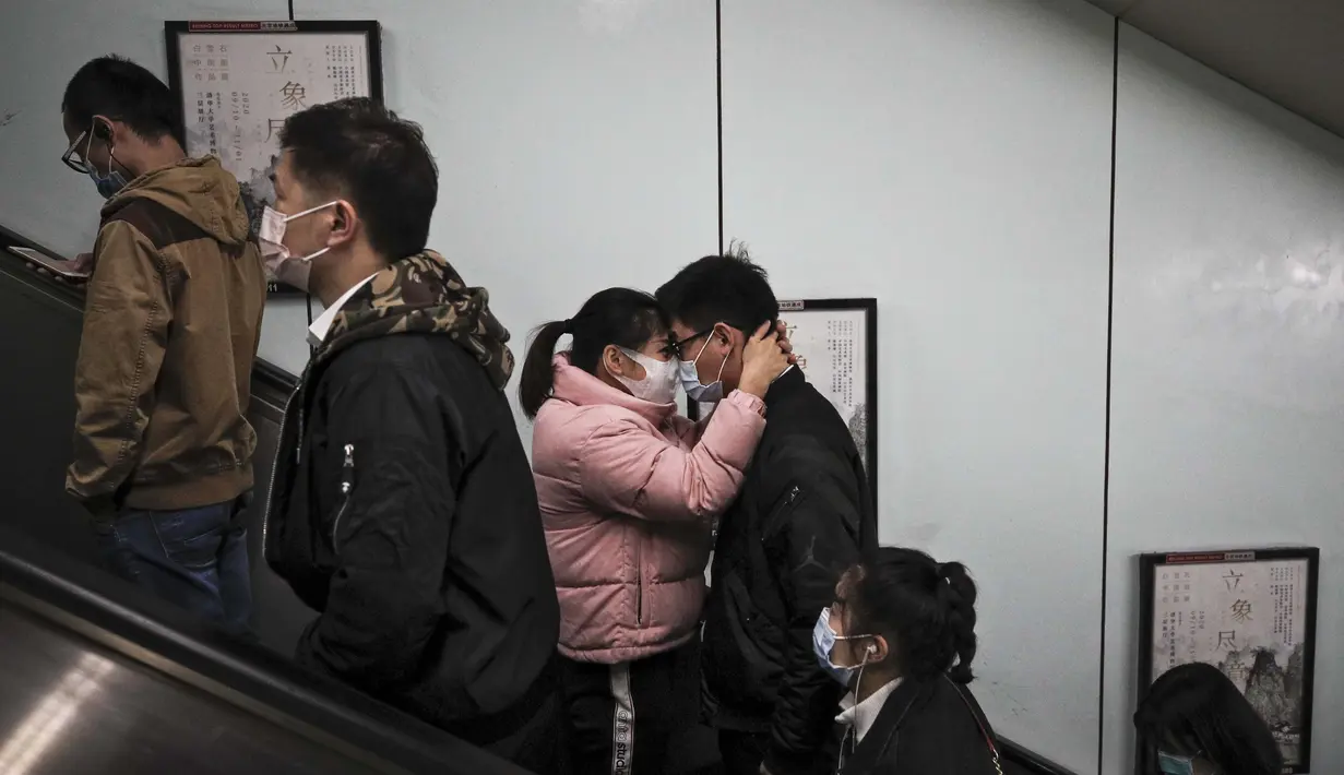 Sepasang suami istri yang mengenakan masker untuk membantu mengekang penyebaran virus corona berpelukan saat mereka keluar dari stasiun kereta bawah tanah pada jam sibuk pagi hari di Beijing, Kamis (29/10/2020). (AP Photo / Andy Wong)