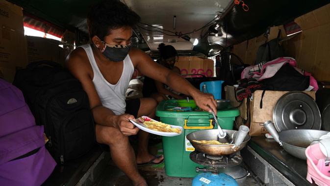 Daniel Flores memasak makan siang di dalam jeepney mereka yang berfungsi sebagai rumah sementara di Manila, 12 Agustus 2020. Angkutan ikonik di Filipina itu belum dapat mengangkut penumpang sejak Maret akibat lockdown Covid-19 yang membuat jutaan orang kehilangan pekerjaan. (Ted ALJIBE/AFP)