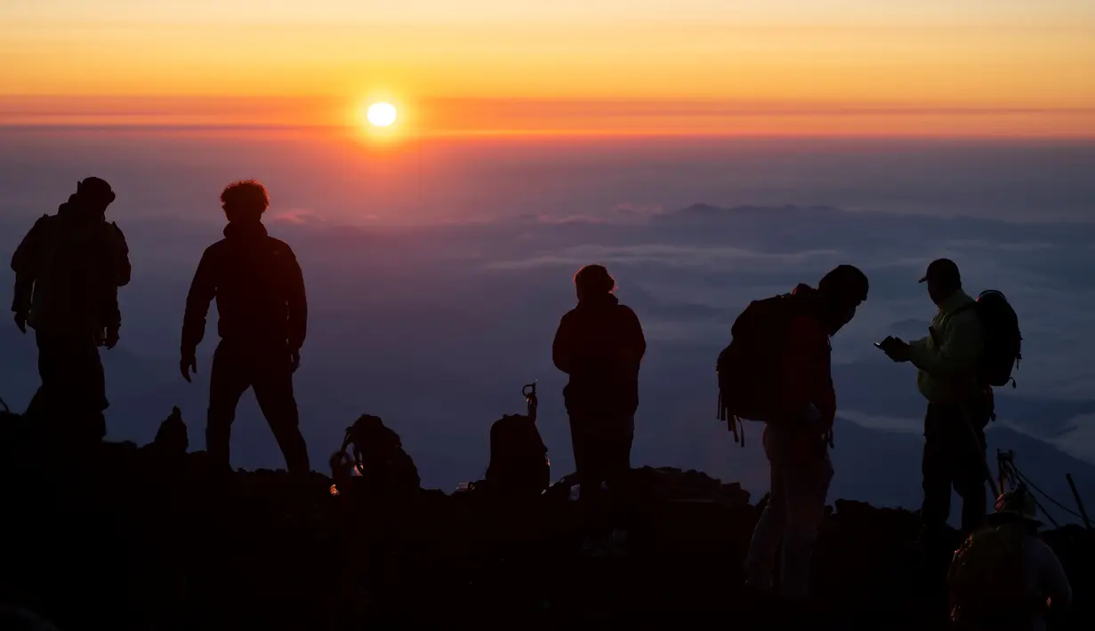 Foto pada 19 Juli 2021 menunjukkan orang-orang menyaksikan matahari terbit dari puncak Gunung Fuji, barat Tokyo. Mendaki Gunung Fuji bukan hal yang mudah, tetapi pemandangan matahari terbit di atas lautan awan adalah hadiah indah bagi yang mencapai puncak tertinggi di Jepang. (Charly TRIBALLEAU/AFP)