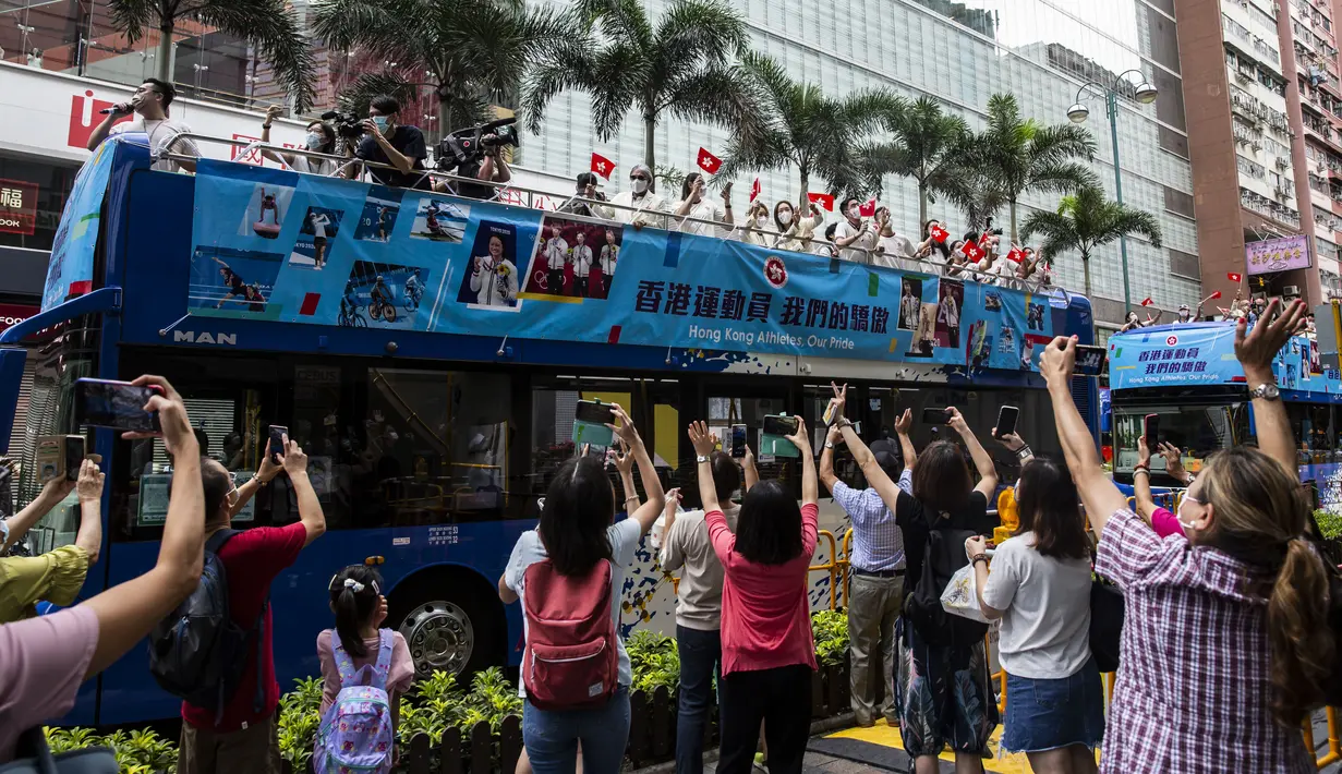 Anggota delegasi Olimpiade Hong Kong mengibarkan bendera selama parade bus, setelah Olimpiade Tokyo 2020, di Hong Kong, Kamis (19/8/2021). Hong Kong yang memiliki 46 atlet perwakilan pada Olimpiade Tokyo 2020 berhasil mengumpulkan satu emas, dua perak dan tiga perunggu. (ISAAC LAWRENCE/AFP)