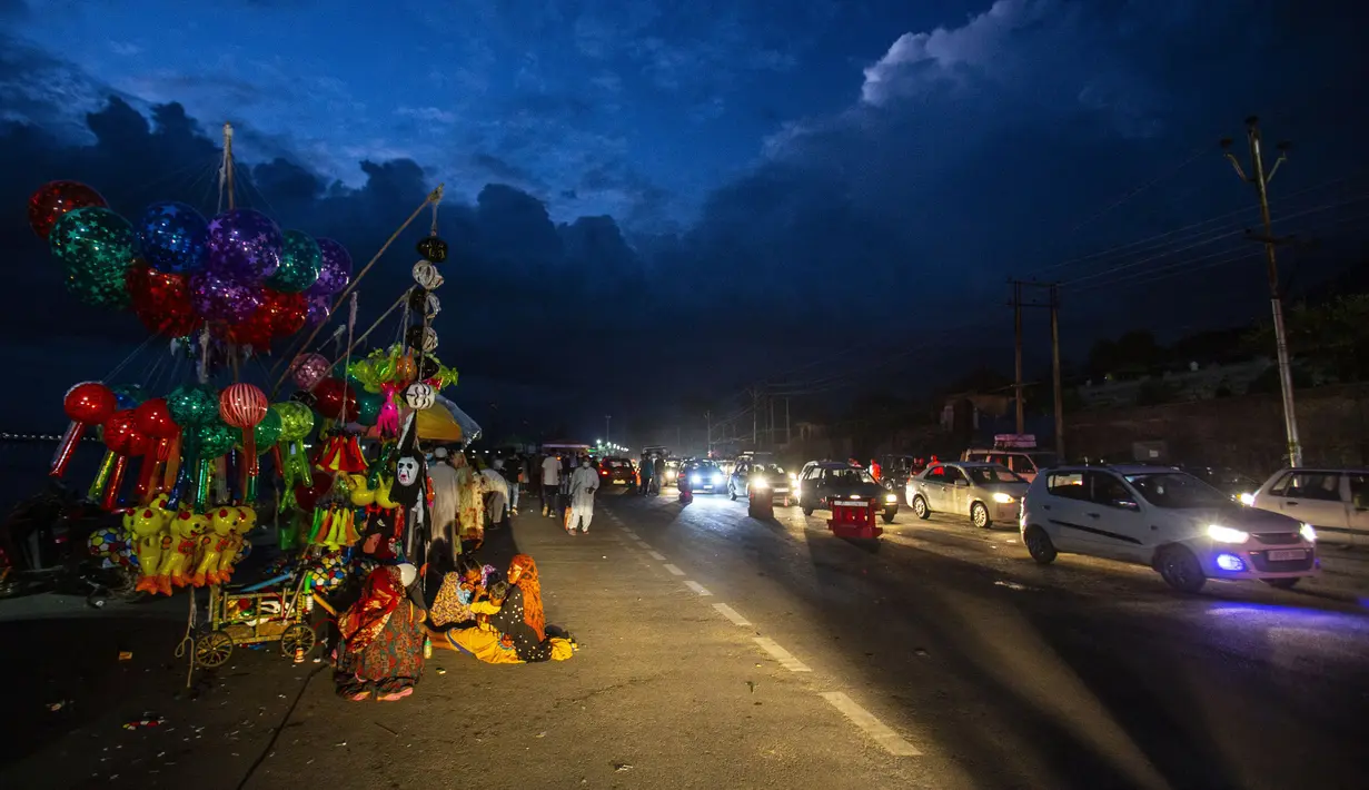 Sebuah keluarga migran menjual balon di pinggir jalan saat awan monsun berkumpul di atas Srinagar, Kashmir yang dikuasai India, Minggu (1/8/2021). Di Sepanjang tepi Danau Dal terdapat Ghate yang merupakan tempat bersandarnya Shikara. (AP Photo/Mukhtar Khan)