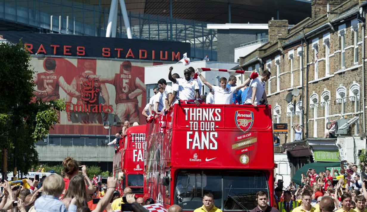 Dari atas bus, para pemain Arsenal melambaikan tangan kepada penggemar fanatik mereka saat parade kemenangan yang dimulai dari depan stadion Emirates, London, Inggris, (18/5/2014). (AFP PHOTO/Oliver Will)