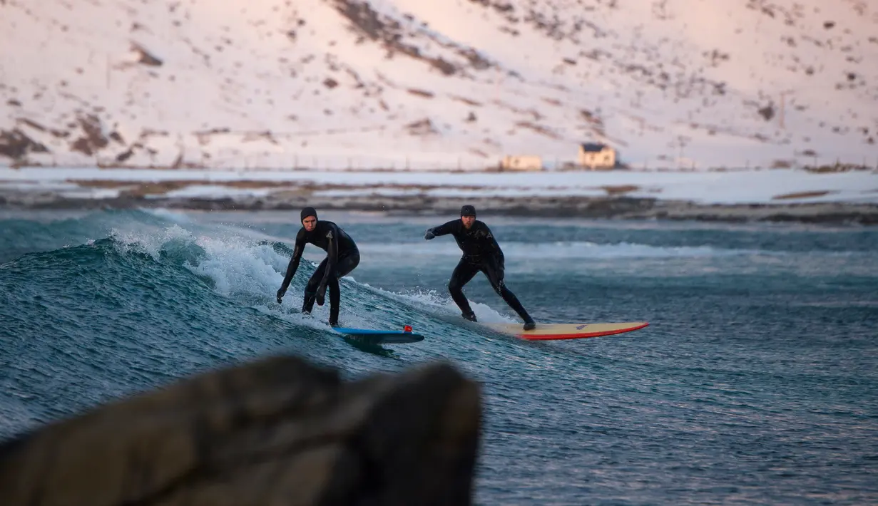 Dua peselancar beraksi melawan ombak yang datang di pantai bersalju Flackstad di Kepulauan Lofoten, Lingkar Arktik, pada 12 Maret 2016. Suhu laut mencapai 5 derajat celcius dan suhu udara hingga 0 derajat celcius. (AFP/Olivier Morin)