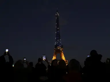 Warga memotret Menara Eiffel yang diterangi warna bendera Ukraina di Paris (25/2/2022). Pasukan Rusia menyerang ibu kota Ukraina pada Jumat (25/2) dengan tembakan dan ledakan dalam invasi ke negara demokratis yang memicu kekhawatiran perang yang lebih luas di Eropa. (AP Photo/Adrienne Surprenant)