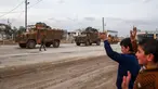 Sejumlah anak-anak melambaikan tangan ke iring-iringan pasukan lapis baja Turki (APC) yang melewati persimpangan perbatasan Bab al-Salamah antara Suriah dan Turki di utara provinsi Aleppo (21/1). (AFP/ Nazeer al-Khatib)
