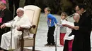 Seorang anak laki-laki dan perempuan bermain di sekitar Paus Fransiskus dalam audensi mingguan di Vatikan, Rabu (28/11). Paus Fransiskus sedang berbicara di depan audiensi ketika bocah laki-laki naik ke atas panggung. (Vincenzo PINTO/AFP)