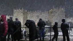 Orang-orang berjalan saat badai salju di sebelah Gerbang Damaskus di Kota Tua Yerusalem, Rabu (26/1/2022). Hujan salju yang jarang melanda sebagian wilayah Israel dan Tepi Barat, menutup sekolah dan bisnis. (AP Photo/Mahmoud Illean)