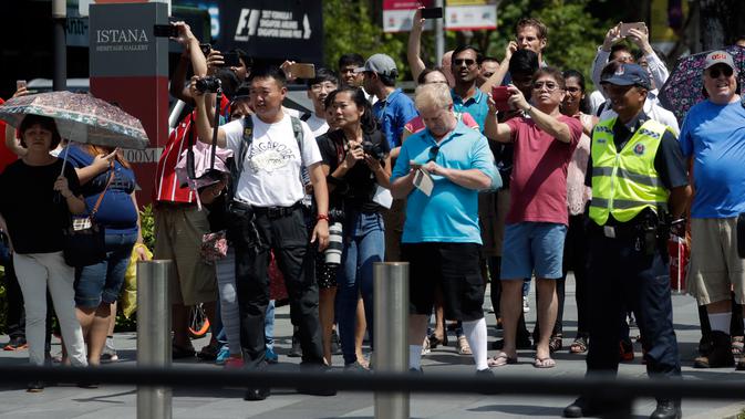 Kerumunan orang melihat iring-iringan mobil Presiden AS, Donald Trump melintasi Orchard Road menuju kediaman resmi PM Lee Hsien Loong di Istana Singapura, Senin (11/6). Trump berkendara menggunakan limosin berbendera Stars and Stripes. (AP/Joseph Nair)