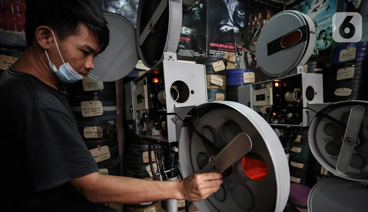Adul (29) membersihkan alat pemutar film seluloid 35mm untuk pertunjukan layar tancap di gudang rumahnya  di Jakarta, Rabu (28/4/2021).Bicara soal industri layar tancap tidak lepas dari keberadaan perlatan dan film seluloid 35mm yang menjadi nadi pertunjukan layar tancap.  (Liputan6.com/Johan Tallo)