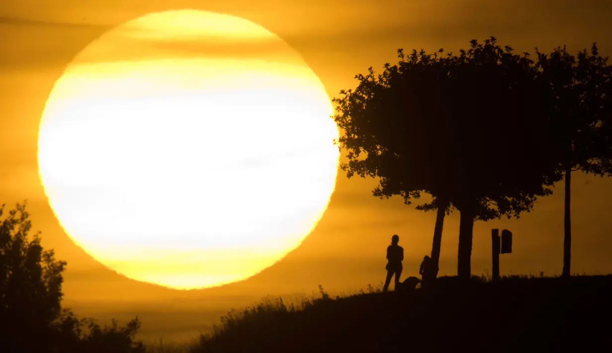 Orang-orang terlihat siluet saat berjalan-jalan selama matahari terbenam di bukit Kronberg di Hannover, Jerman utara (6/8). (AP Photo/Julian Stratenschulte)