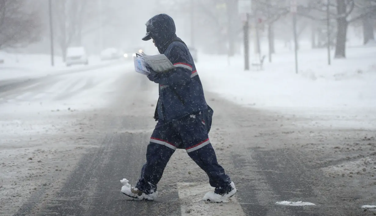 Sebuah operator Pos AS berjalan melintasi persimpangan Downing Street dan Louisiana saat badai musim dingin menjatuhkan beberapa inci salju di Denver (25/1/2022). (AP Photo/David Zalubowski)