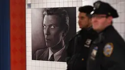 Dua petugas NYPD berdiri dekat instalasi seni yang memajang gambar David Bowie di stasiun kereta bawah tanah Broadway-Lafayette, New York City, 19 April 2018. Instalasi seni yang berlangsung hingga 13 Mei mendatang. (ANGELA WEISS/AFP)