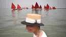 Seorang wanita berdiri di depan anggota asosiasi pelayaran budaya yang berlayar dalam acara Regatta Merah di Venesia, Italia, Minggu (20/6/2021). Red Regatta mengumpulkan lebih dari 50 perahu tradisional Venesia dengan 52 layar warna merah. (MARCO BERTORELLO/AFP)