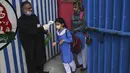 Seorang guru memeriksa suhu tubuh siswa ketika mereka tiba di sebuah sekolah di Lahore (16/9/2021). Pemerintah Pakistan membuka kembali lembaga pendidikan yang ditutup sebagai tindakan pencegahan untuk mengekang penyebaran virus corona Covid-19. (AFP/Arif Ali)