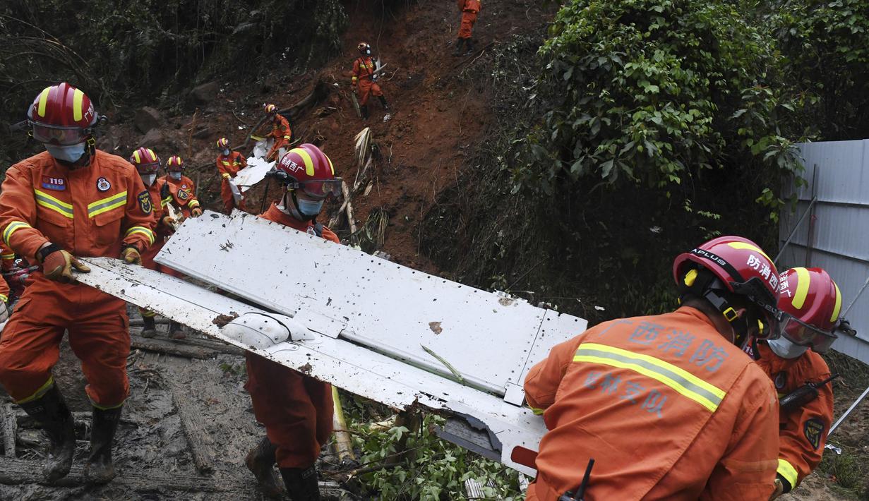 Petugas membawa puing di lokasi kecelakaan pesawat China Eastern di Kabupaten Tengxian di Daerah Otonomi Guangxi Zhuang, China selatan (24/3/2022). Area pencarian diperluas dalam pencarian korban dan kotak hitam kedua pesawat dengan 132 orang itu. (Lu Boan/Xinhua via AP)