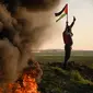 Warga Palestina membakar ban dan mengibarkan bendera nasional saat protes terhadap serangan militer Israel terhadap kamp pengungsi Jenin di perbatasan Israel-Palestina, sebelah timur Kota Gaza, 26 Januari 2023. Presiden Palestina Mahmoud Abbas mengumumkan masa berkabung tiga hari, di mana bendera akan dikibarkan setengah tiang. (AP Photo/Fatima Shbair)