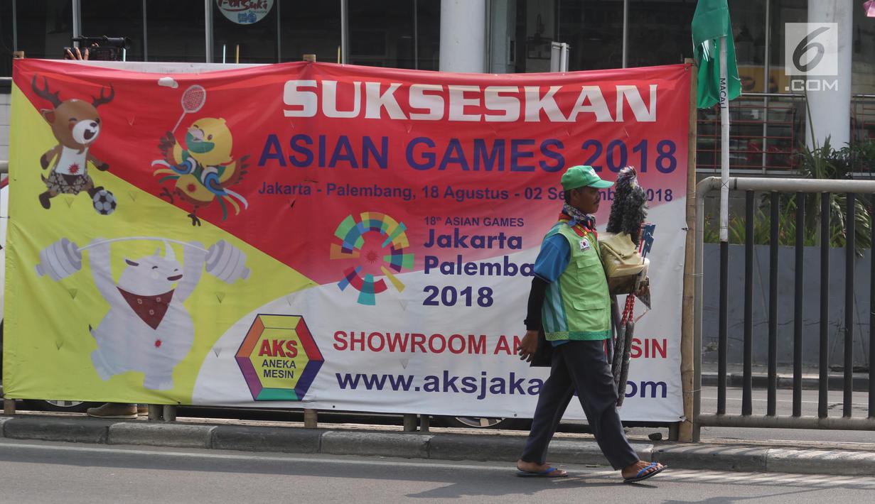 Pedagang melintas dekat bendera negara peserta Asian Games 2018 yang diikat di tiang bambu di pagar pembatas Jalan Pluit Selatan Raya, Jakarta, Kamis (19/7). Pemasangan merupakan inisiatif warga dalam memeriahkan Asian Games. (Liputan6.com/Arya Manggala)