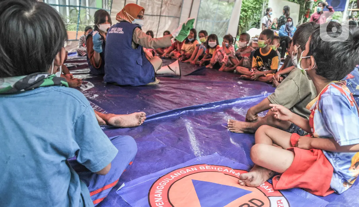 Anak-anak mendengarkan dongeng yang dikisahkan petugas di tenda pengungsian di SDN 09 Kebon Kosong, Kemayoran, Jakarta, Selasa (31/8/2021). Kegiatan bertujuan menghilangkan trauma atau rasa takut serta kebosanan anak-anak korban kebakaran saat berada di pengungsian. (merdeka.com/Iqbal S. Nugroho)