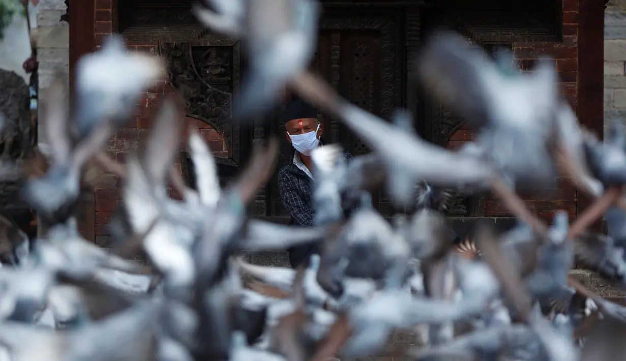 Seorang lelaki tua mengenakan masker saat beristirahat di sebuah kuil yang penuh dengan merpati, Basantapur Durbar Square, Kathmandu, Nepal, Rabu (22/7/2020). Pemerintah Nepal mengakhiri lockdown setelah sebelumnya diberlakukan untuk mengendalikan penyebaran COVID-19. (AP Photo/Niranjan Shrestha)