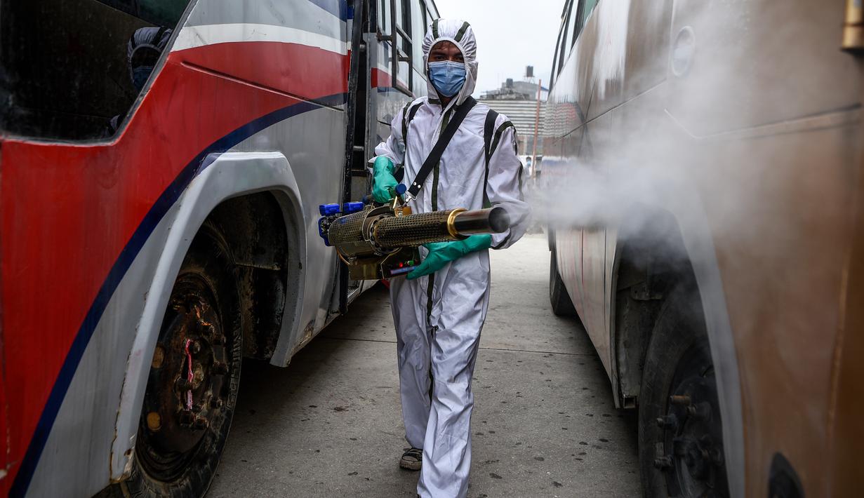 Pekerja yang mengenakan Alat Pelindung Diri (APD) menyemprotkan disinfektan pada bagian luar bus di Kathmandu, Kamis (17/9/2020). Pemerintah Nepal melonggarkan pembatasan yang diberlakukan sebagai tindakan pencegahan terhadap virus corona pada transportasi umum jarak jauh. (PRAKASH MATHEMA/AFP)