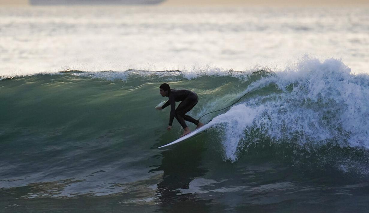 Seorang peselancar mengendarai ombak di Huntington Beach, California, Amerika Serikat, 12 Januari 2022. Peselancar di seluruh California Selatan berbondong-bondong ke daerah pantai saat gelombang ombak besar memasuki wilayah tersebut. (AP Photo/Ashley Landis)
