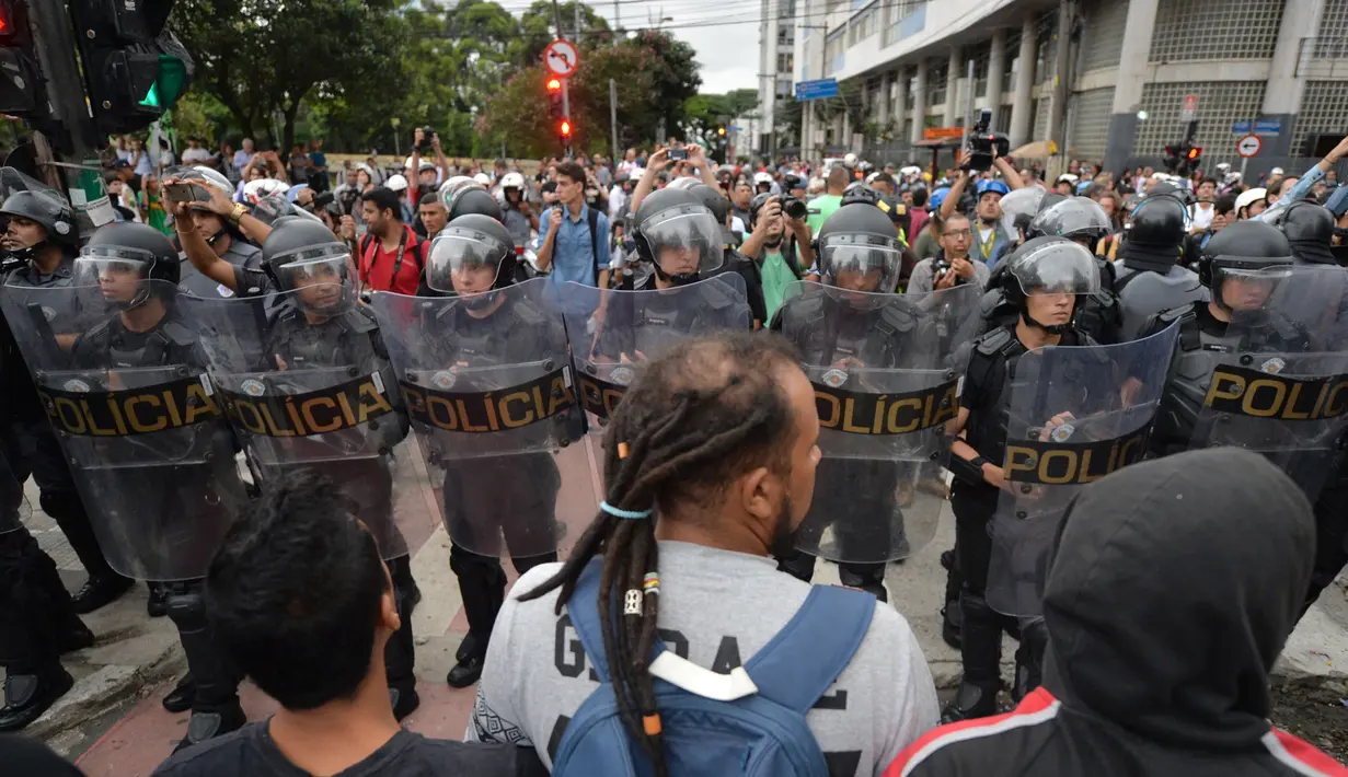 Massa berhadapan dengan polisi anti huru hara saat memprotes kenaikan tarif bus di Sao Paulo, Brasil, Selasa (12/1). Mereka protes karena di tengah krisis ekonomi, tarif transportasi angkutan bus justru naik. (AFP PHOTO/NELSON Almeida)