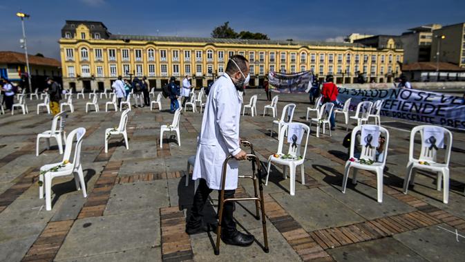 Seorang dokter melewati bangku dengan nama petugas kesehatan yang meninggal karena COVID-19 selama aksi protes terhadap sistem kesehatan di Bogota, Senin (26/10/2020). Kolombia pada Sabtu, 24 Oktober, melampaui satu juta kasus COVID-19 yang dikonfirmasi sejak dimulainya pandemi. (Juan BARRETO/AFP)