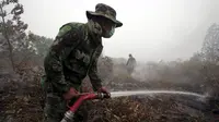 Seorang anggota TNI menyemprotkan air ke lahan gambut yang terbakar di Kampar, Riau, Jumat (11/9/2015). Sekitar 10.000 anggota TNI diterjunkan untuk membantu memadamkan kebakaran lahan yang terjadi di Sumatera. (REUTERS/YT Haryono)