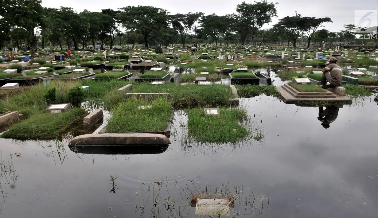 Seorang penjaga makam duduk di kompleks TPU Semper yang terendam banjir, Jakarta, Selasa (4/12). (Merdeka.com/Iqbal S. Nugroho)