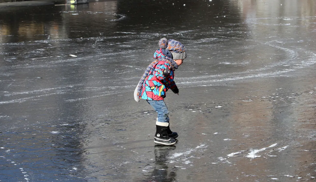 Seorang anak asyik berseluncur melintasi permukaan kanal Prinsengracht yang membeku di Amsterdam, Belanda, Jumat (2/3). Mereka sekarang bisa bermain ice skating di kanal-kanal yang melewati kota. (AP/Mike Corder)