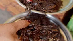 Penjual menyajikan kuliner tarantula goreng di wilayah Skun, Provinsi Kampong Cham, Kamboja, 14 Maret 2018. Tarantula paling enak dibumbui garam dan bawang putih, kemudian digoreng dalam minyak panas. (TANG CHHIN Sothy / AFP)