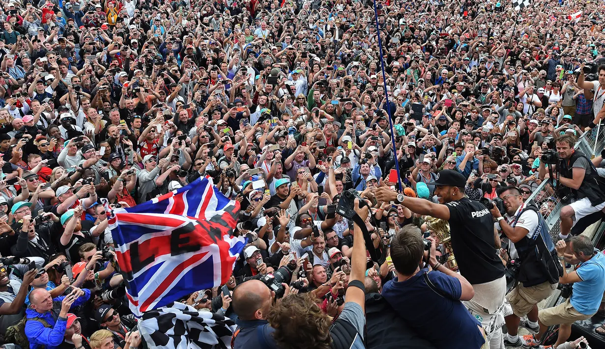 Pembalap Formula 1, Lewis Hamilton merayakan kemenangan bersama pengemarnya usai berlaga di Grand Prix Formula 1 Silverstone di Inggris, (5/7/2015). Hamilton berhasil finish di urutan pertama dengan waktu 1 jam 31 menit 27,729 detik. (Reuters/Stringer)